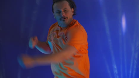 Active-jumping-man-looking-at-the-camera.-Crazy-man-dancing-in-the-neon-light-of-the-ridiculous-dance.-Funny-man-on-a-colored-blue-background.